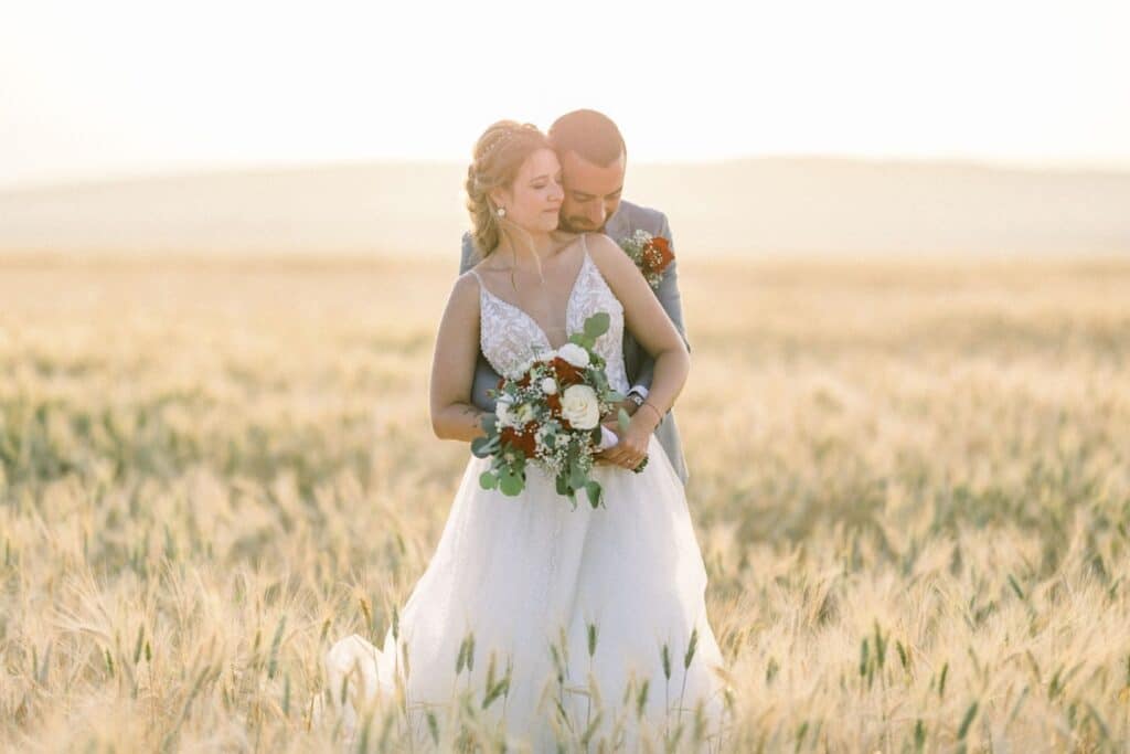 Bride and groom embrace in a golden wheat field.