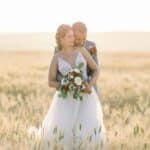 Bride and groom embrace in a golden wheat field.