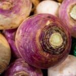 This close-up image showcases turnips, specifically Brassica rapa subsp. rapa varieties, displaying their characteristic bulbous shape and purple-tinged skin. These root vegetables are a staple in many cuisines, offering a slightly peppery flavor. The image highlights the natural textures and colors of the turnips, from the vibrant purple skin to the creamy white flesh. Rich in vitamins C and K, as well as fiber, turnips are a nutritious addition to various dishes.